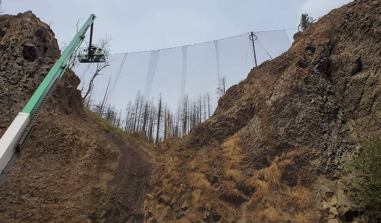 A photo of workers and a crane installing an attenuator fence