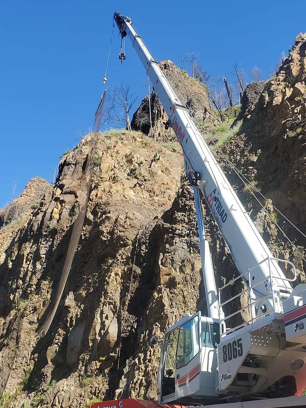 A photo of attenuator mesh being installed on hillside by workers and a crane