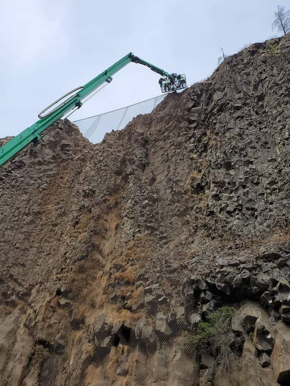 A photo of attenuator mesh being installed on hillside by workers and a crane