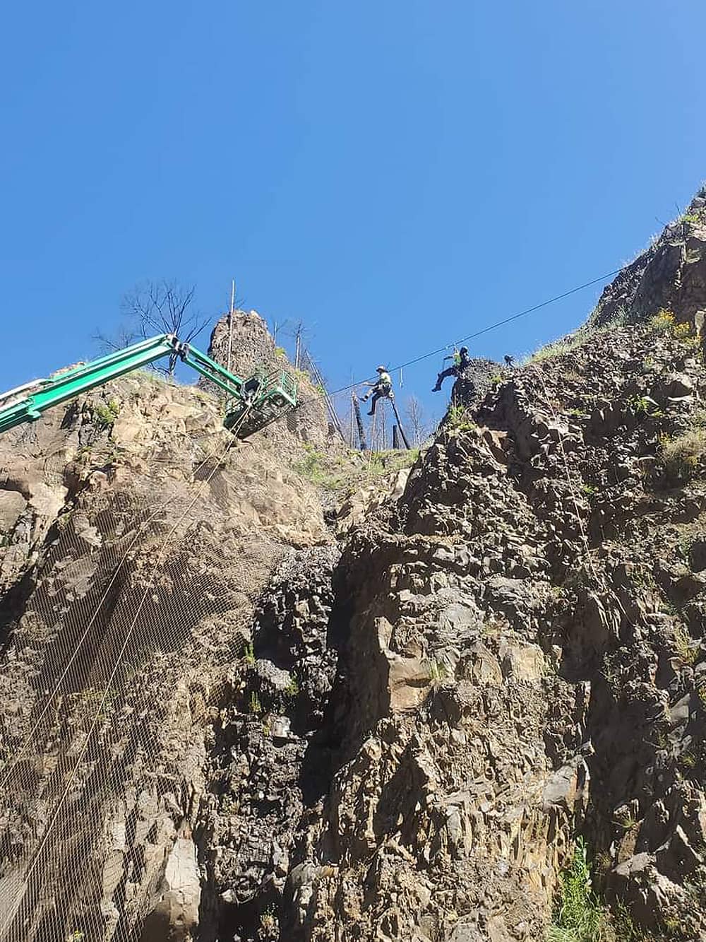 A photo of attenuator mesh being installed on hillside by workers and a crane