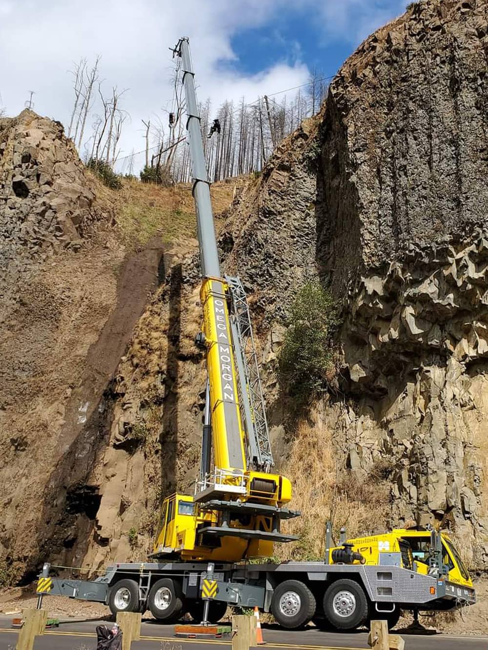 A photo of attenuator mesh being installed on hillside by workers with a crane