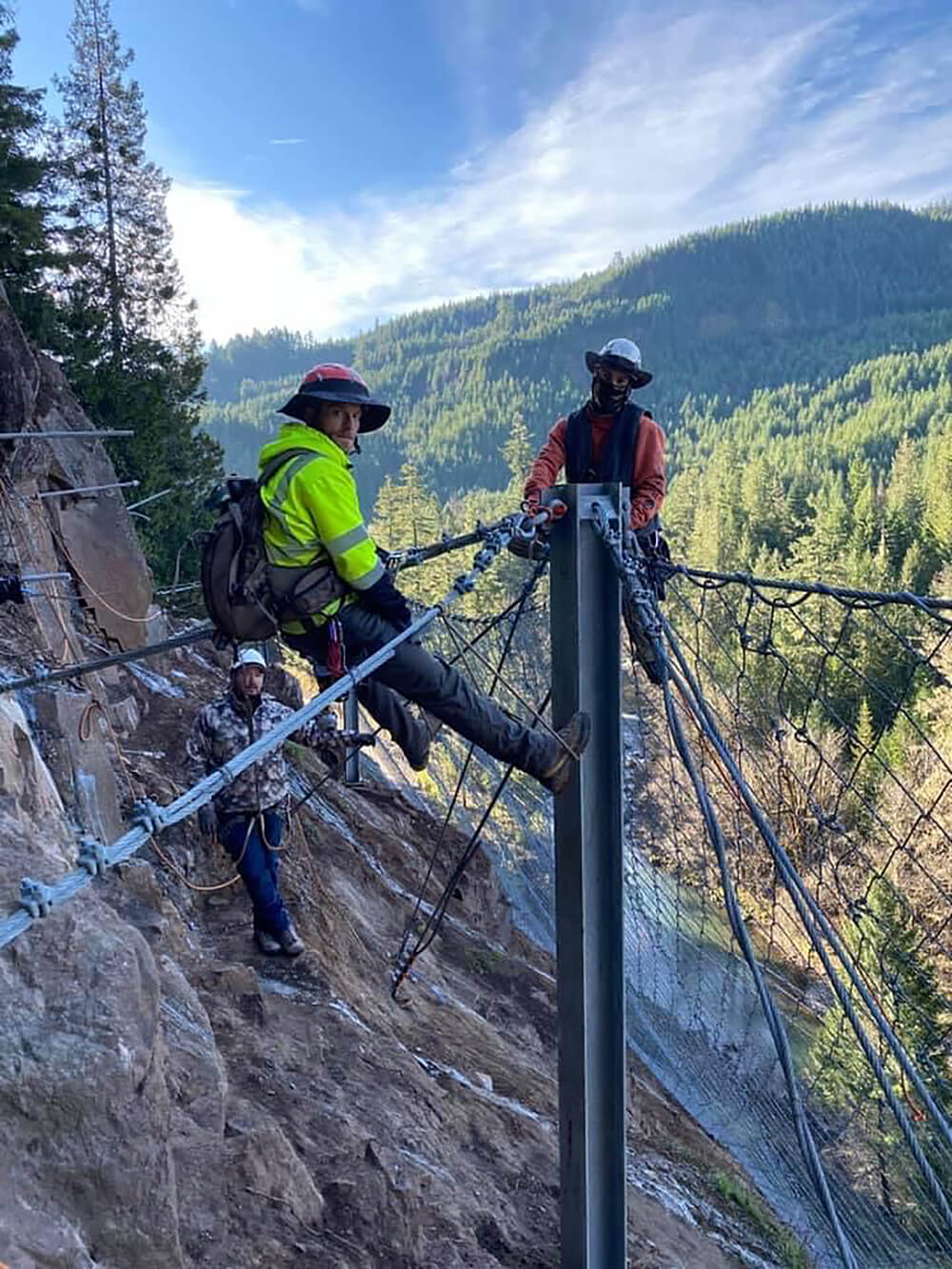 A photo of professionally trained workers installing attenuator mesh on a hillside