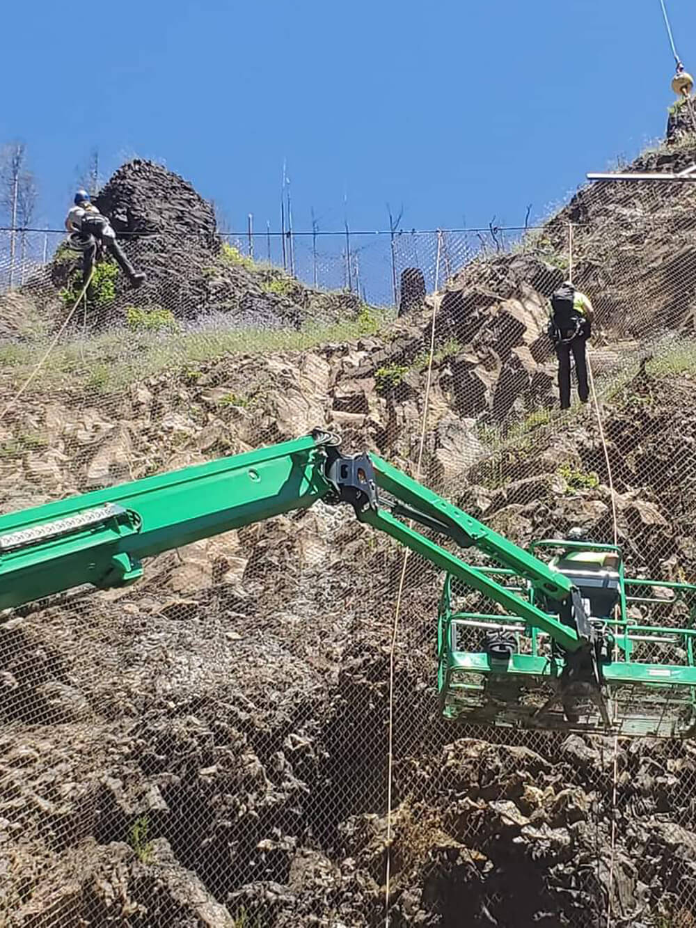 A photo of attenuator mesh being installed on hillside by workers and a crane