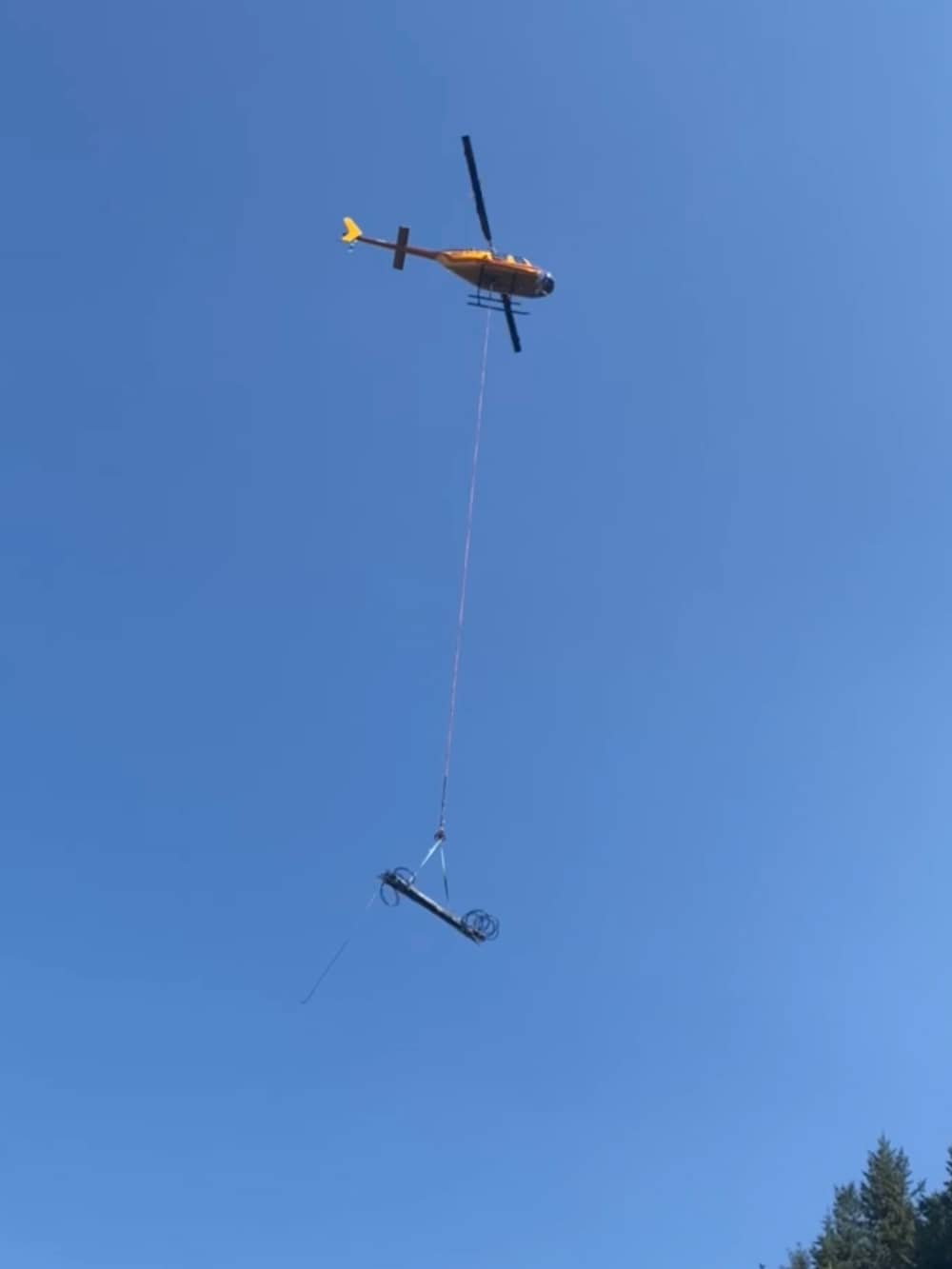 A photo of a helicopter transporting equipment for attenuator mesh to be installed on a hillside