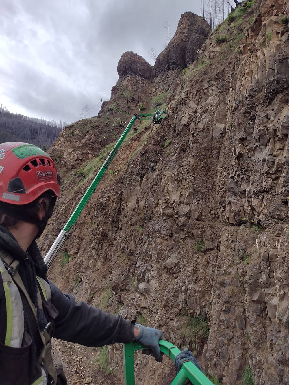 A photo of attenuator mesh being installed on hillside by workers and a crane