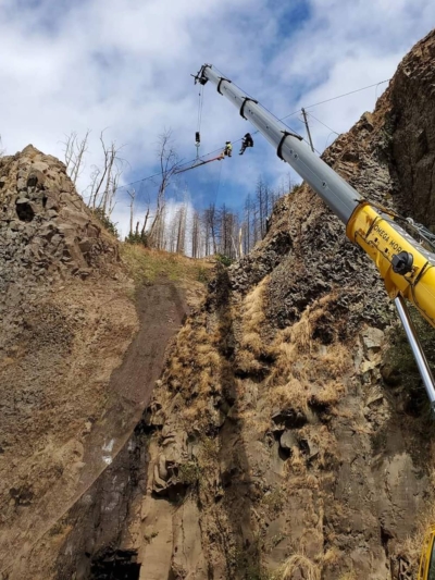 A photo of attenuator mesh being installed on hillside by workers with a crane