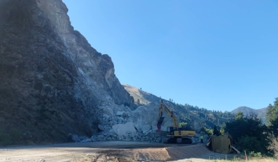 A photo of a large rock landslide over a highway and a cleanup operation in progress