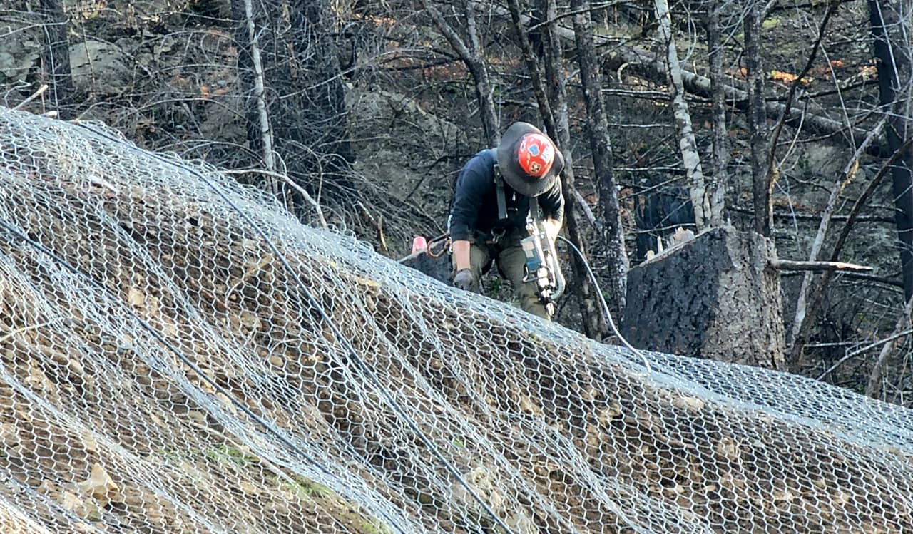 A photo of a trained scaler installing draped mesh over a roadside hill