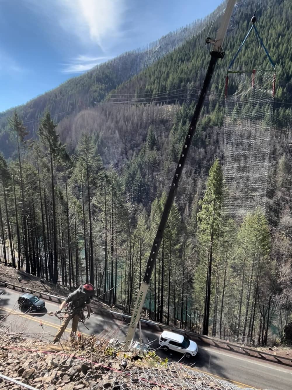 A photo of installing draped mesh over a road cut along a highway