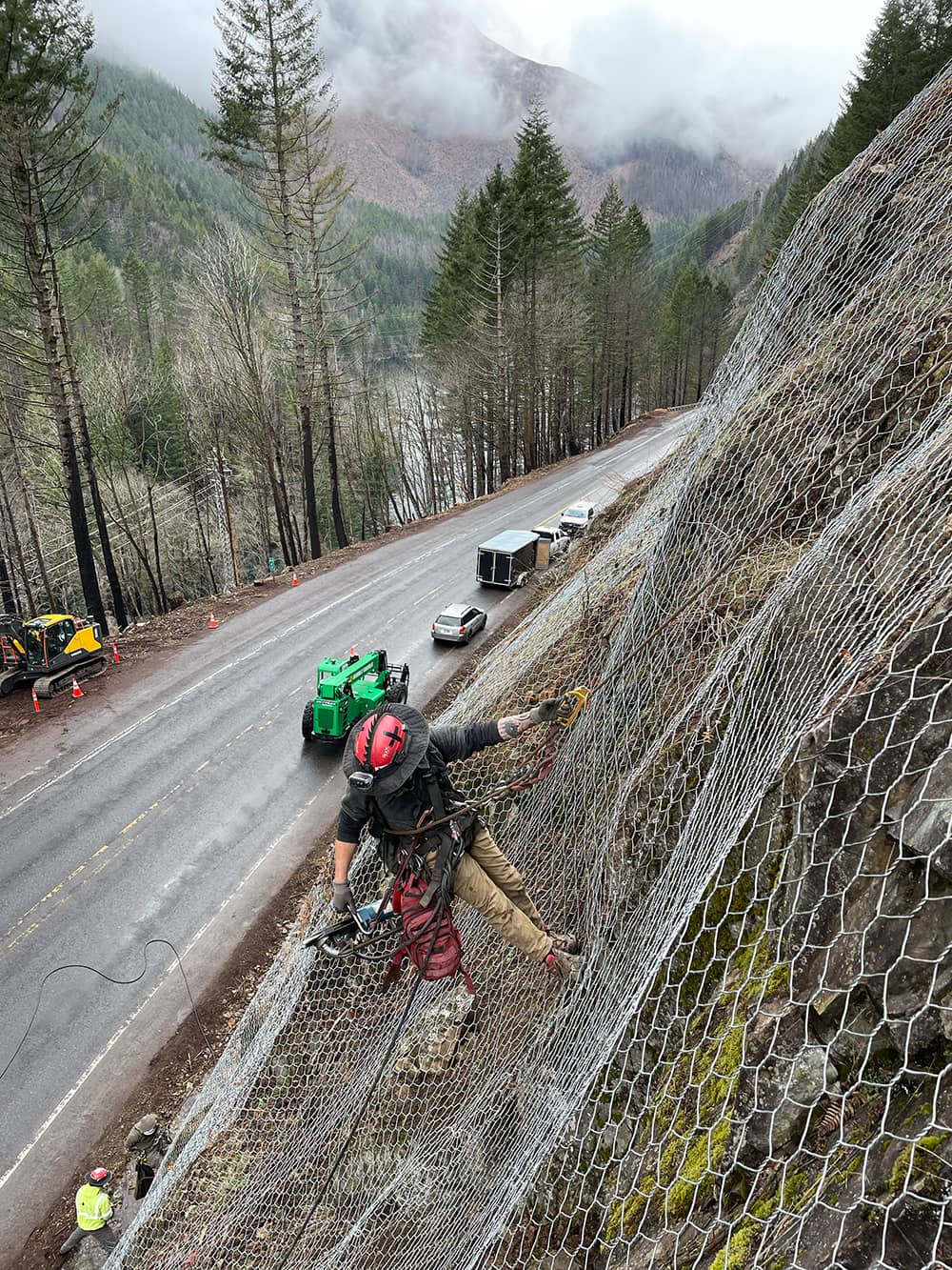 A photo of a trained scaler installing draped mesh over a road cut next to a highway