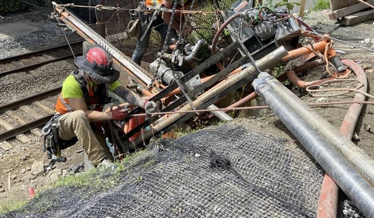 A photo of two men working near railroad tracks with a remote access drill