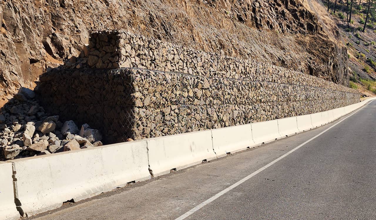 A photo of a mesh and rock protective barrier along a highway