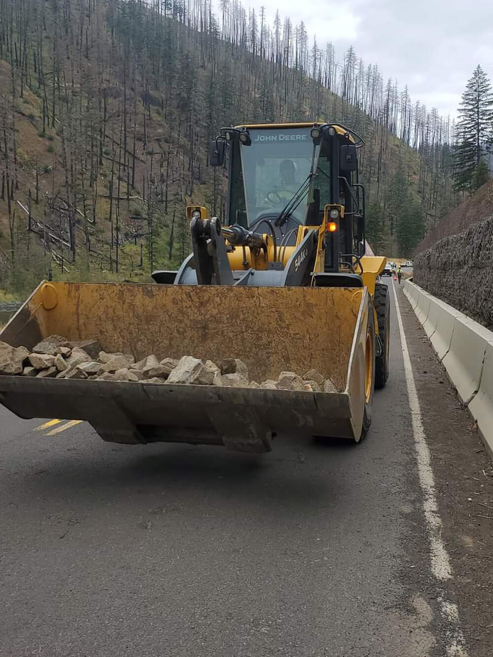 A photo of a bulldozer carrying rock for a protective barrier along a roadside