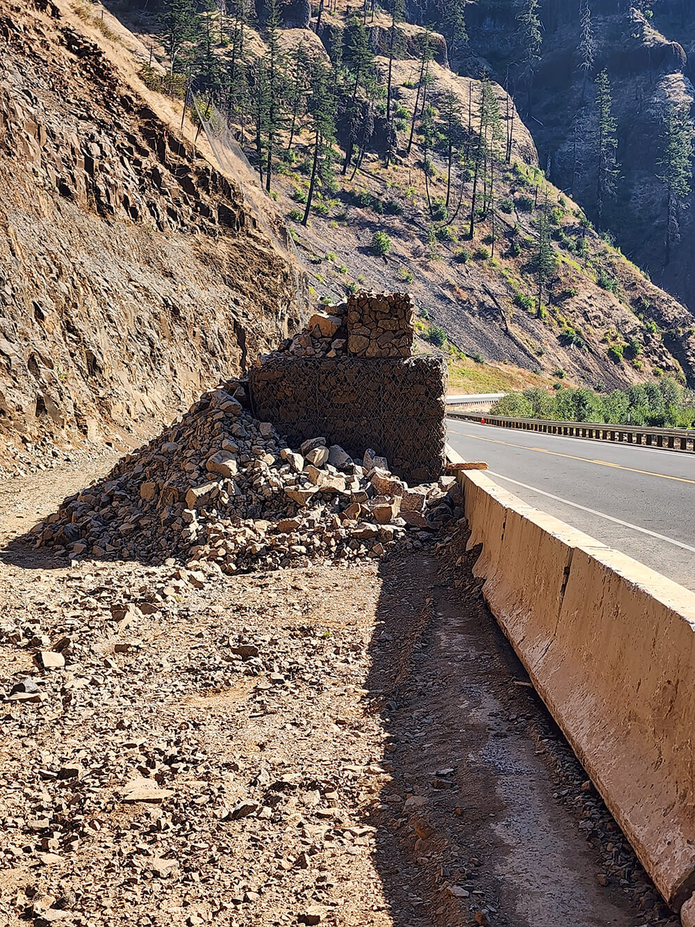 A photo of a mesh and rock protective barrier along a highway