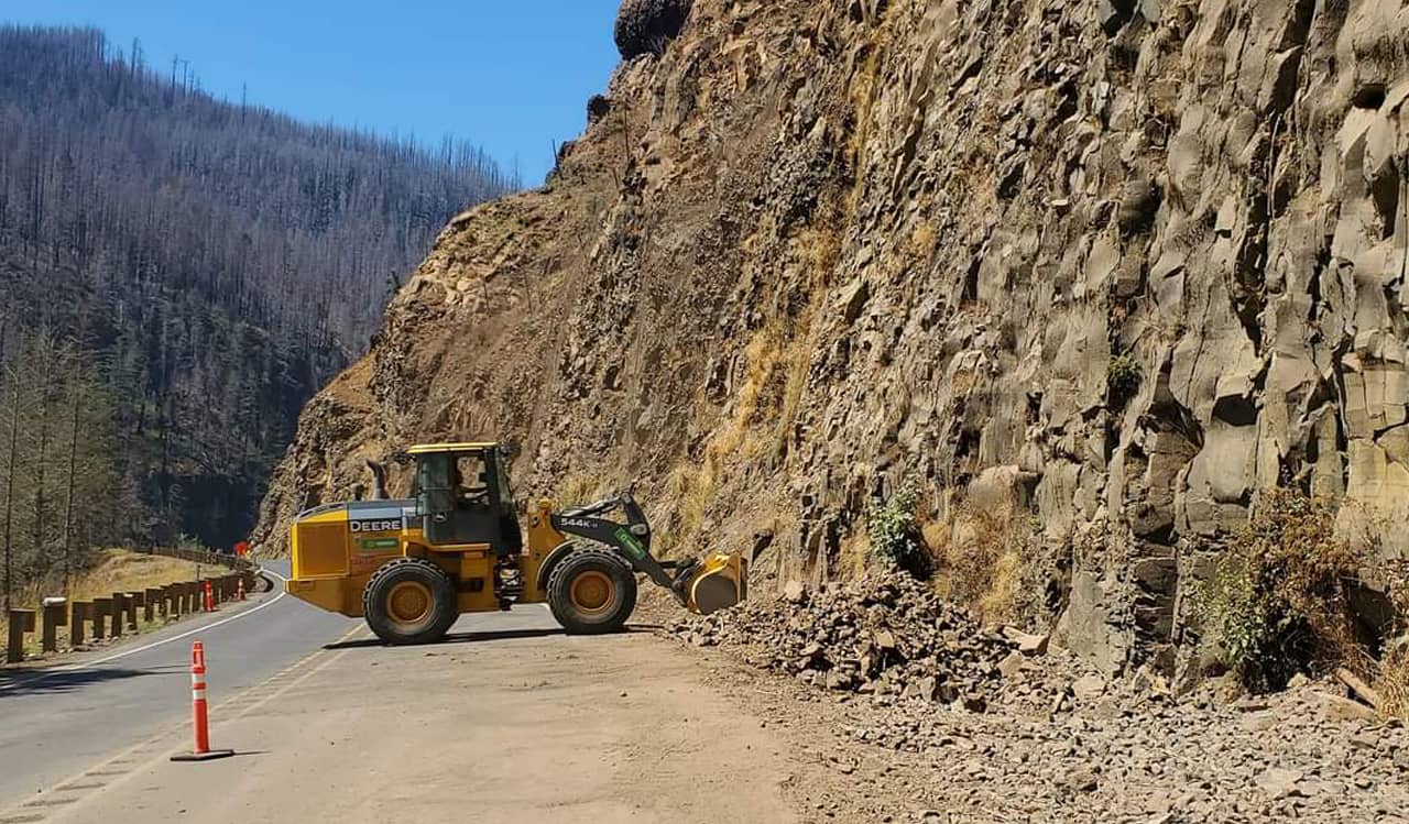 A photo of a bulldozer working on a rock road cut along a road