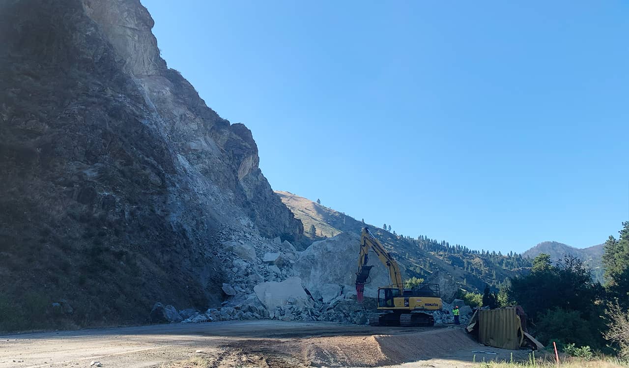 A photo of a large rock landslide over a highway and a cleanup operation in progress
