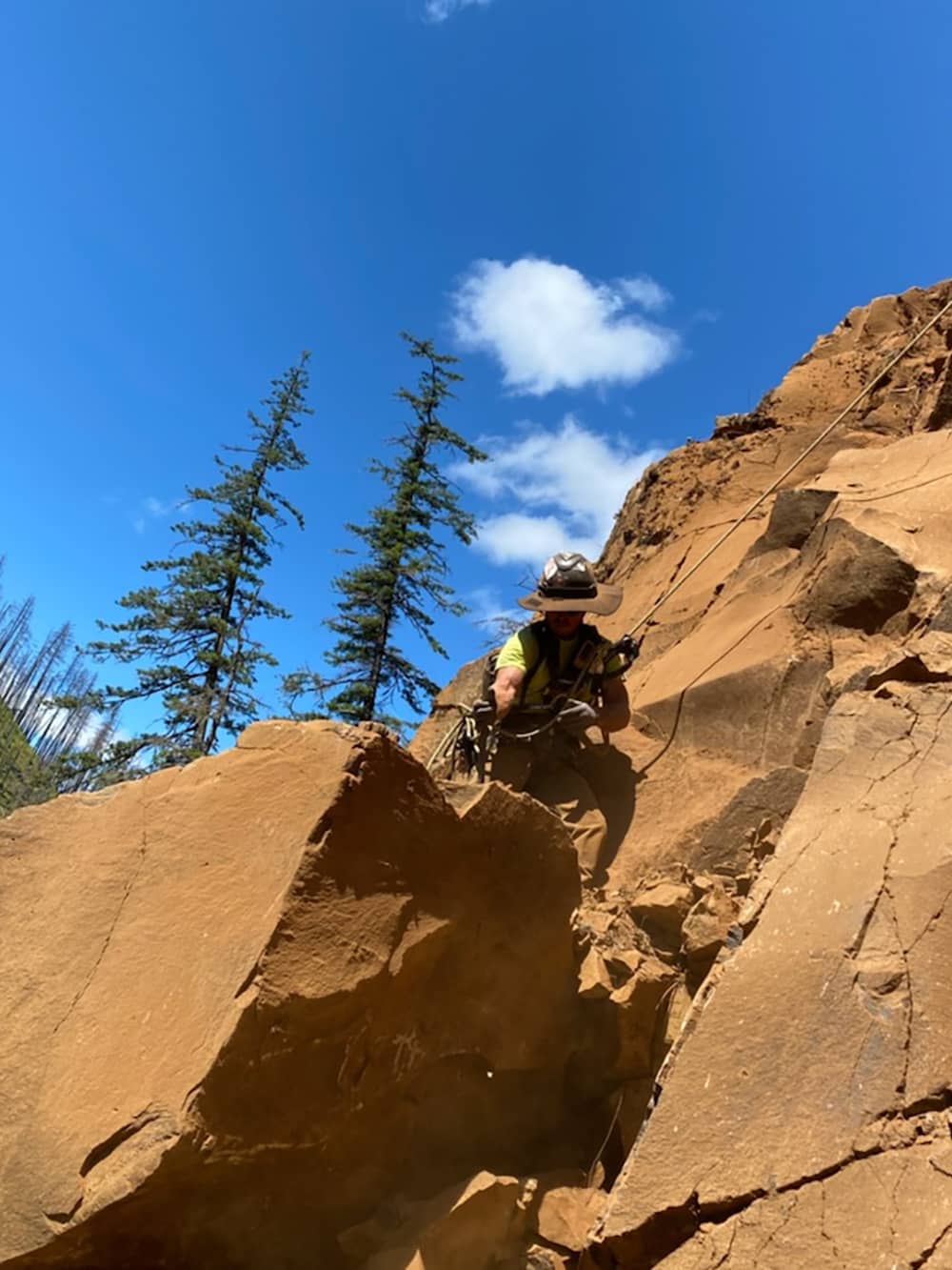 A photo of a trained professional performing rope access and rockfall mitigation work on a rock outcropping