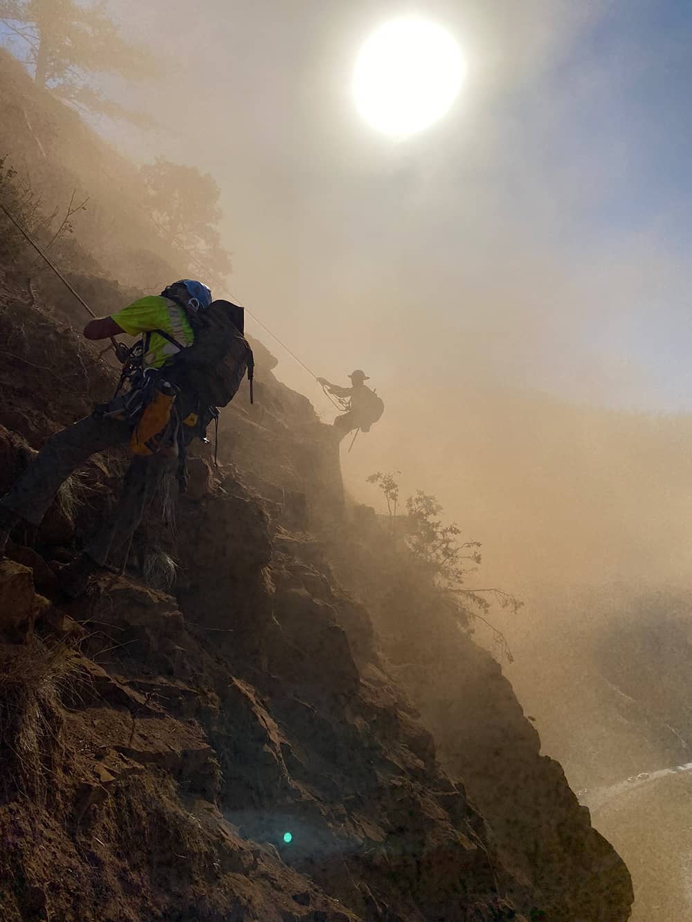 A photo of 2 trained professionals performing rope access and rockfall mitigation work on a road cut near a highway