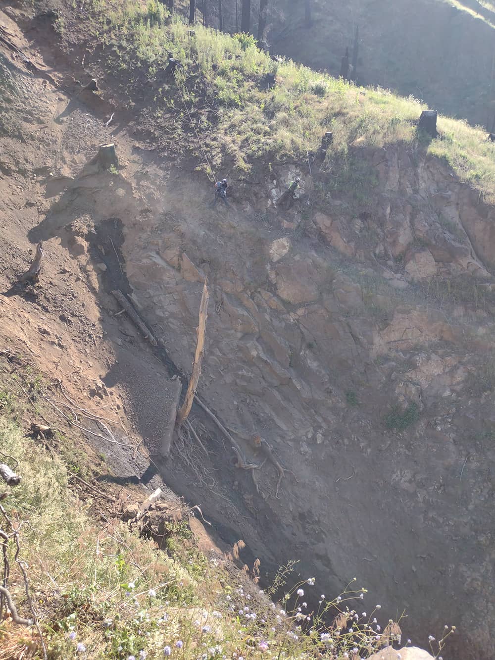 A photo of 2 trained professionals performing rope access and landslide mitigation work