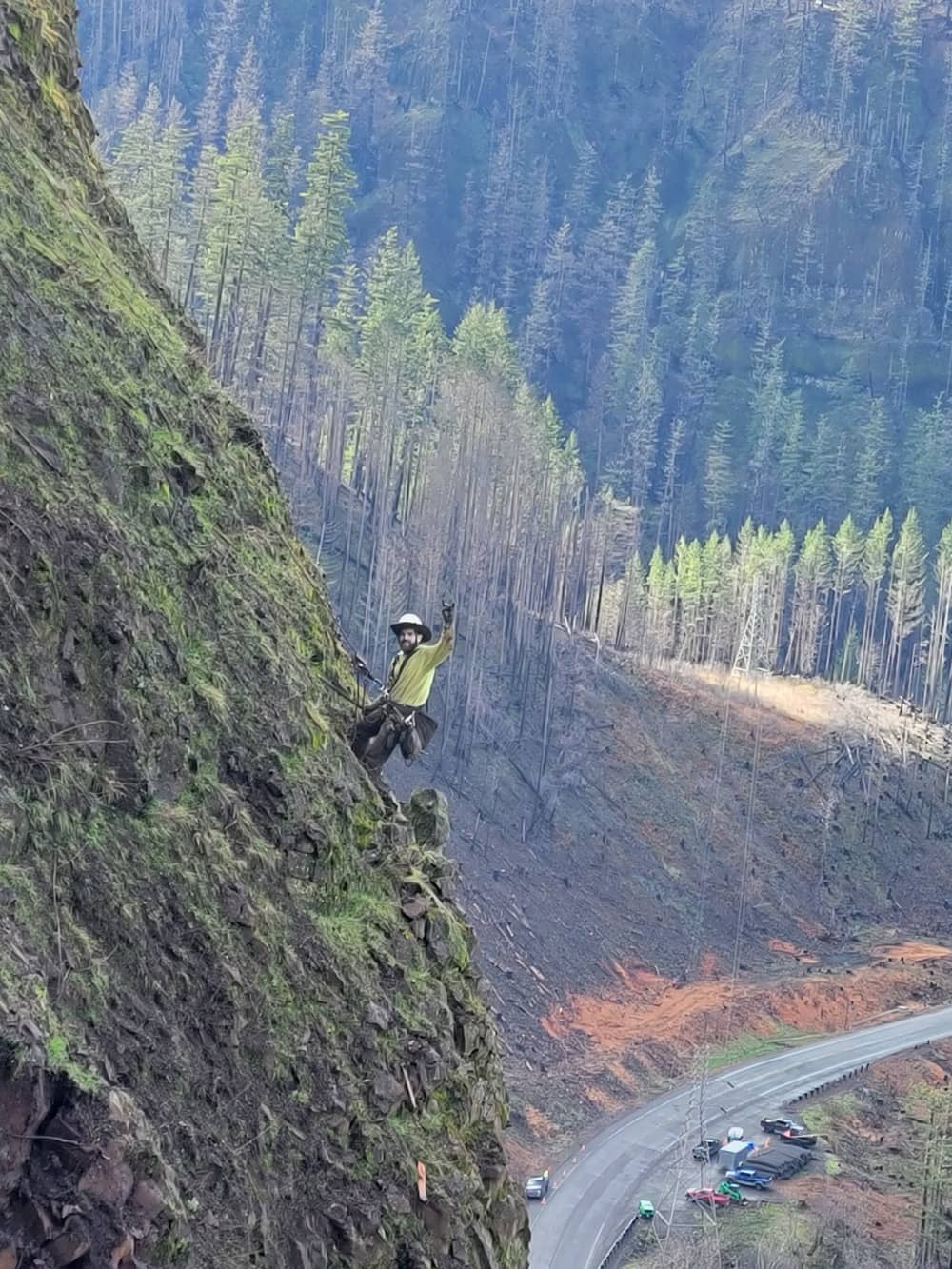 A photo of a trained professional performing rope access work on a road cut near a highway