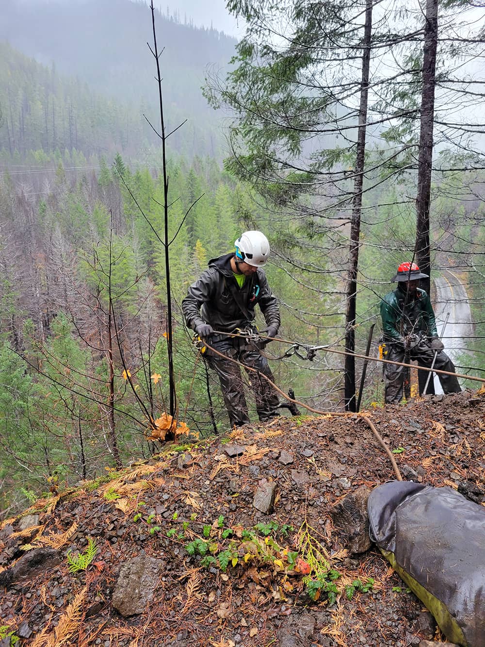 A photo of 2 trained professionals performing rope access and rockfall mitigation work on a hill