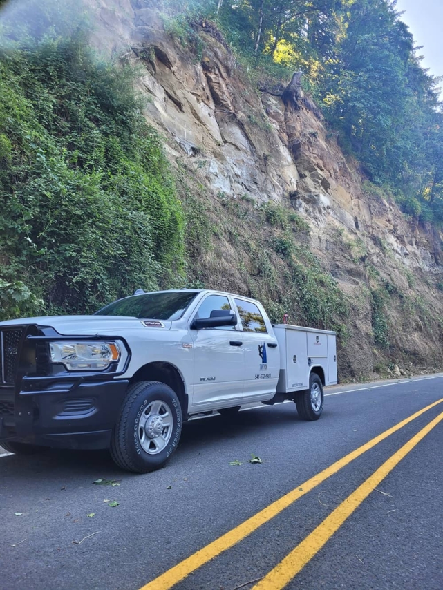 A photo of a white, Triptych Construction truck in front of a highway road cut
